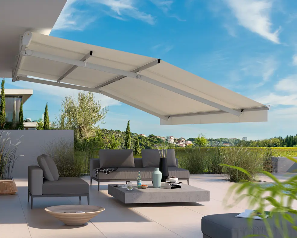 Moderne Terrasse mit grauen Sitzmöbeln unter einem ausgefahrenen weißen Sonnenschutz, im Hintergrund grüne Landschaft und blauer Himmel.