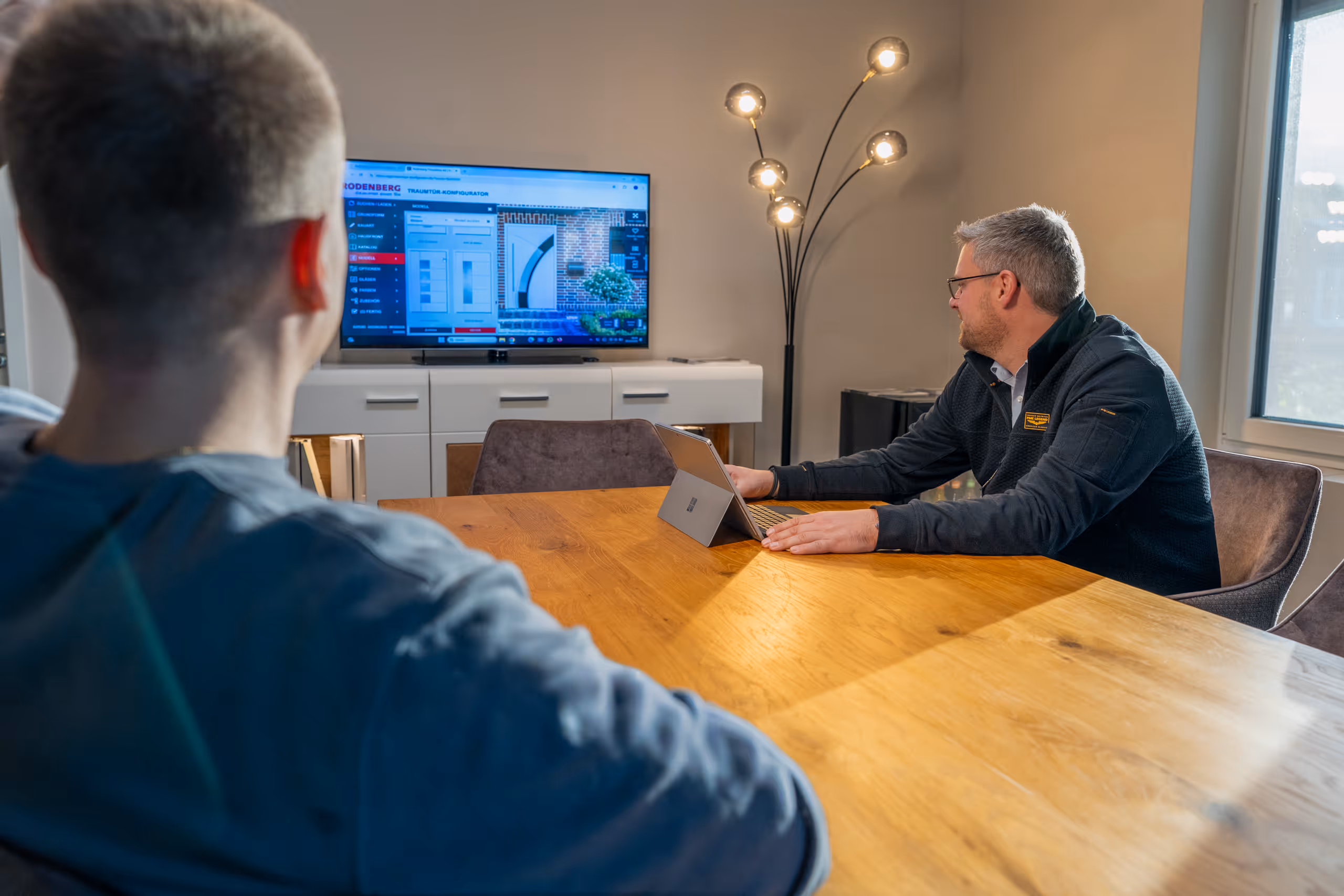 Zwei Männer sitzen an einem Holztisch und sehen auf einen Bildschirm mit Türkonfigurator-Software.