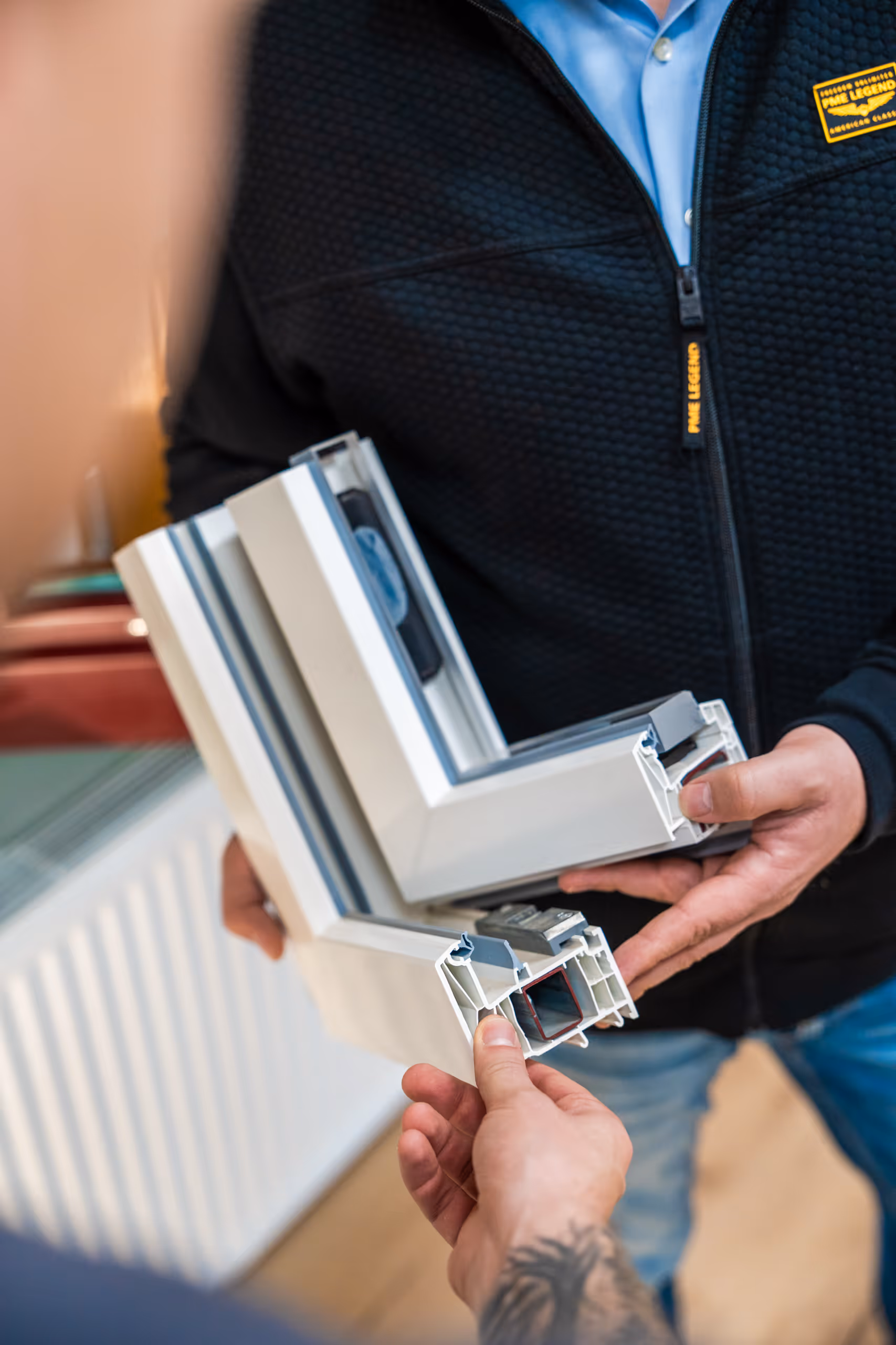 Zwei Personen vergleichen weiße Kunststofffensterprofile in einem Innenraum.