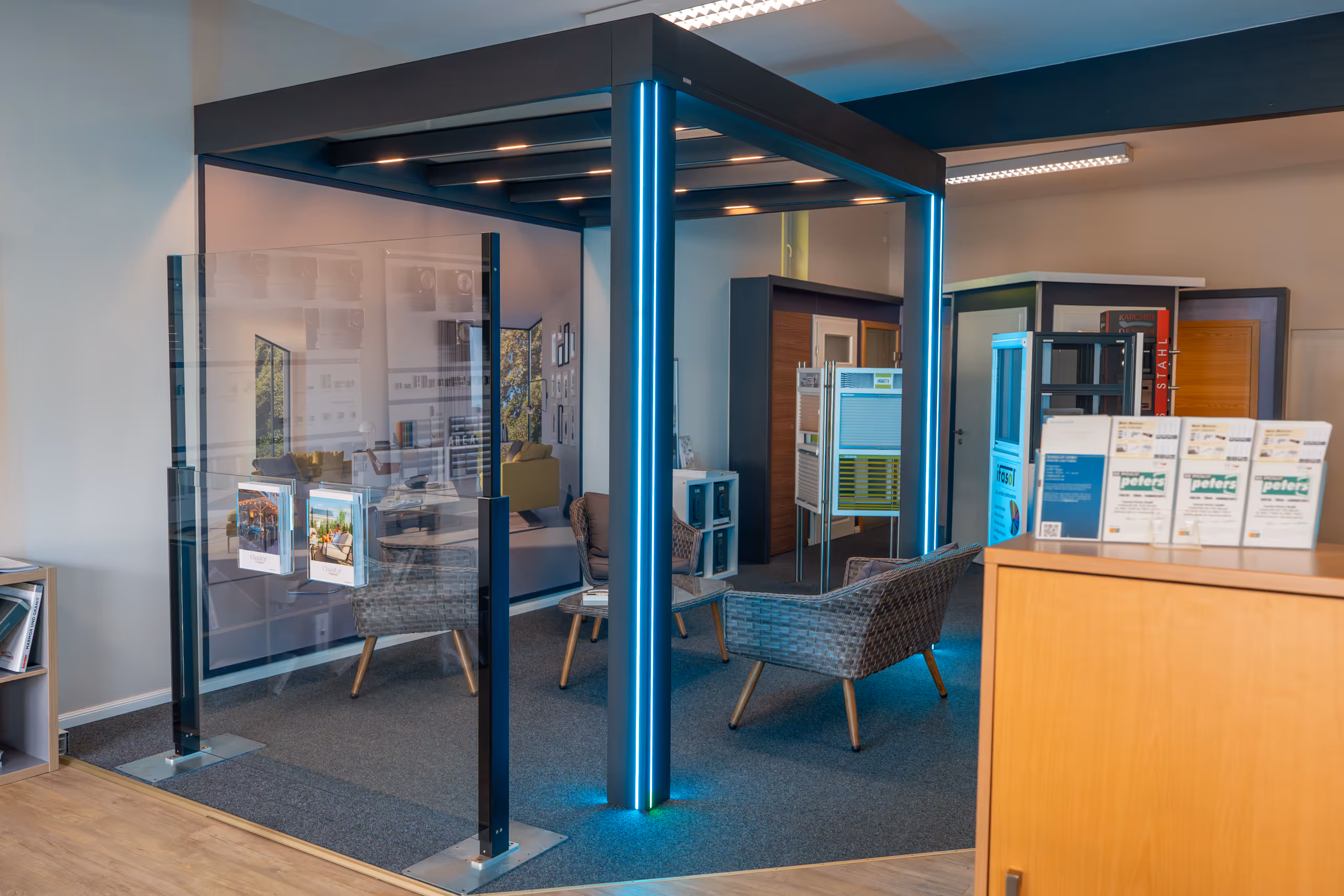 Moderner Ausstellungsbereich mit Sitzmöbeln aus geflochtenem Material und einer beleuchteten Glasstruktur.