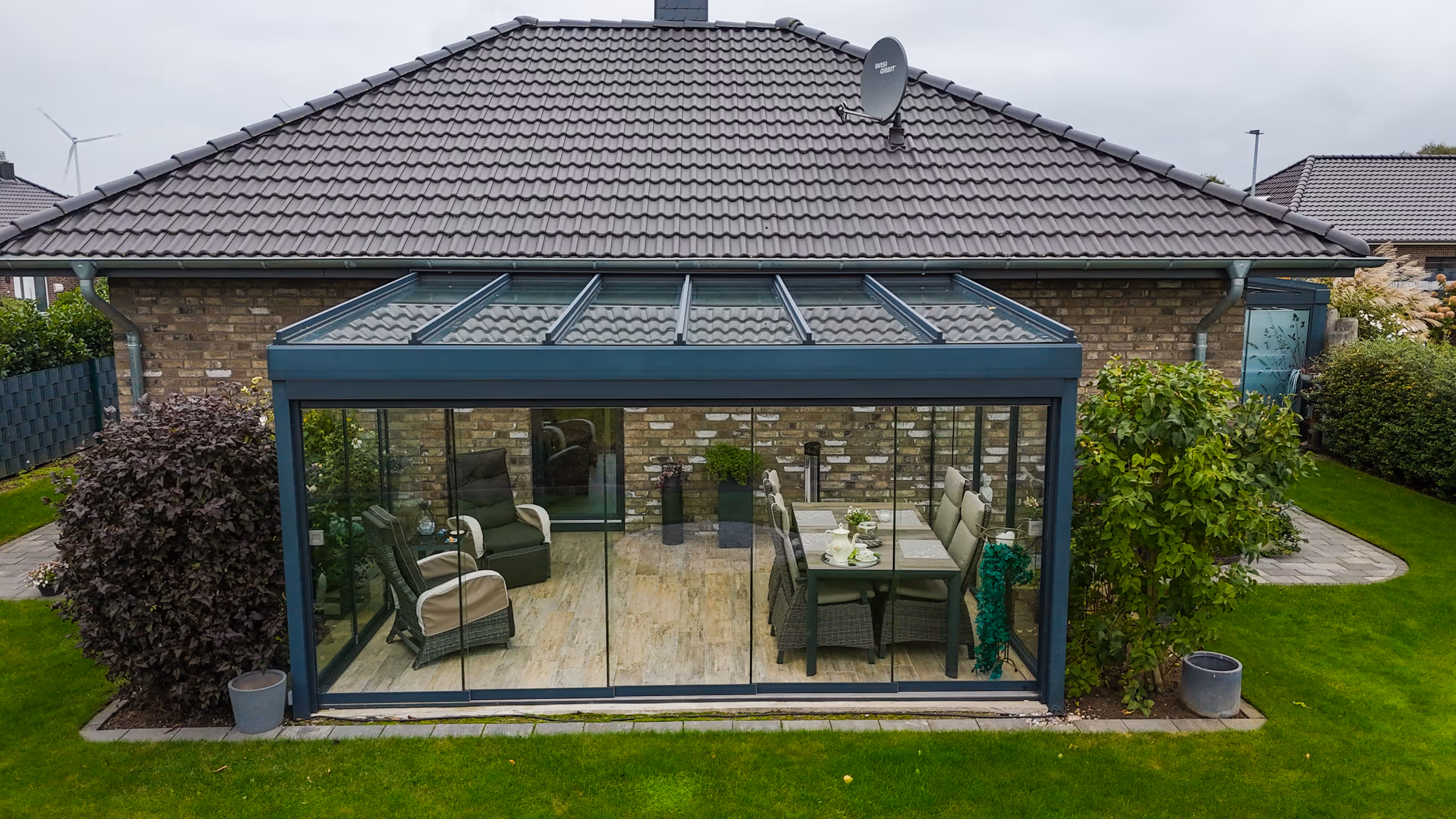 Moderner Wintergarten mit Glaswänden und Glasdach an einem Einfamilienhaus mit Garten.