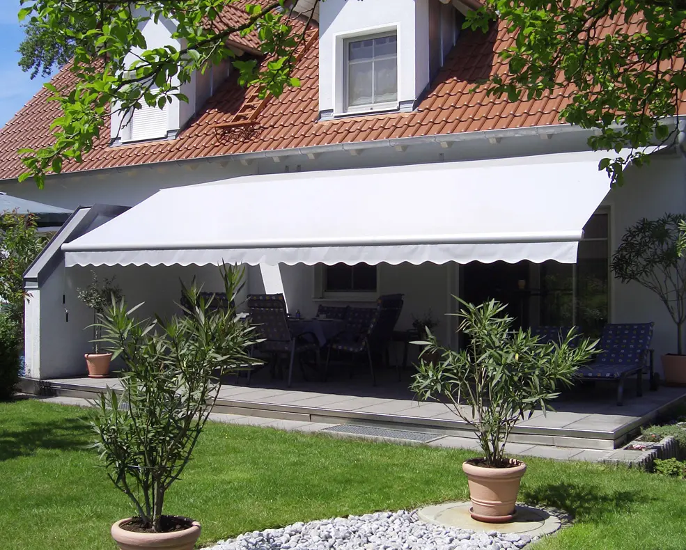 Haus mit rotem Ziegeldach und einer weißen Markise über einer Terrasse mit Gartenmöbeln und Topfpflanzen.