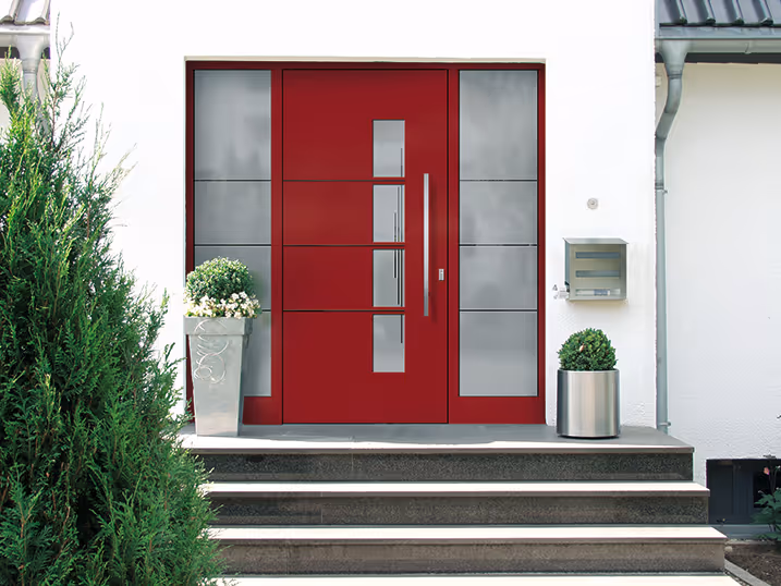 Moderne rote Haustür mit vertikalem Fenster und seitlichen Glaseinsätzen an einem weißen Haus mit Treppenstufen und bepflanzten Blumentöpfen.