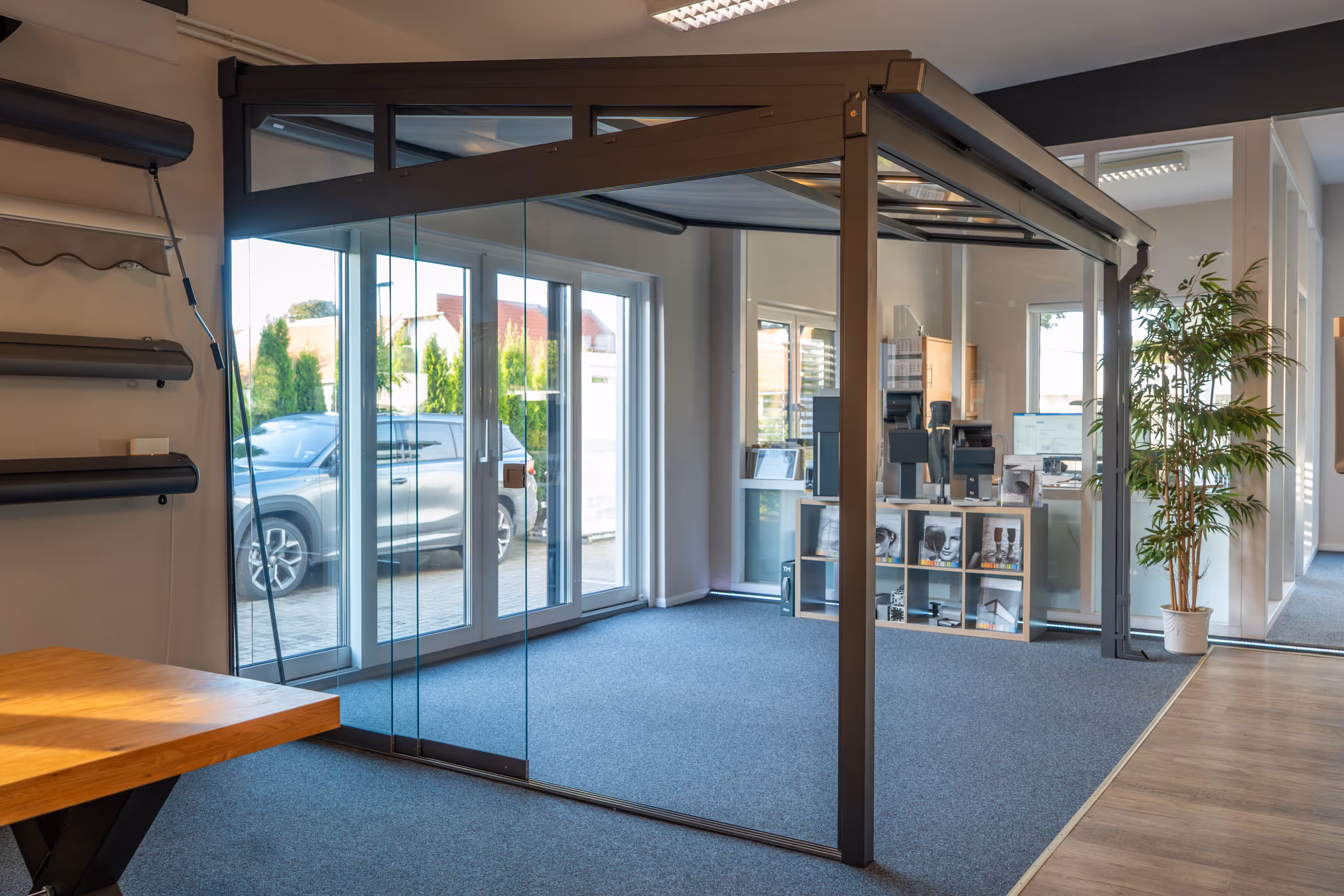 Moderner Ausstellungsraum mit Sitzbereich aus grauen Rattanstühlen und Glastrennwand, beleuchtet mit blauen LED-Lichtern.