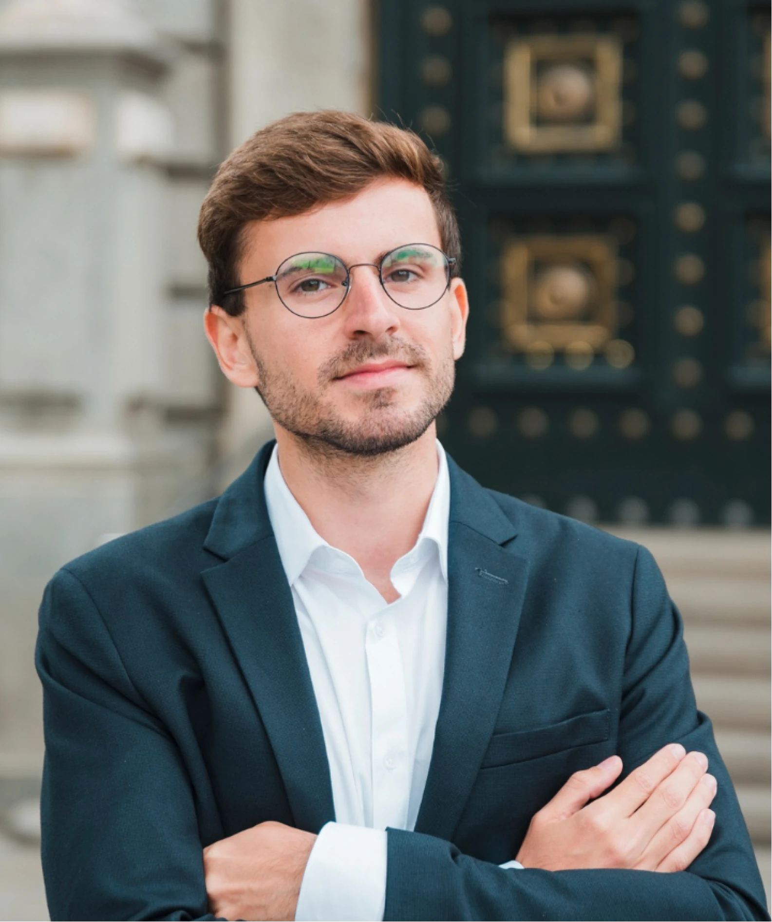 A man in a suit and glasses standing with his arms crossed.