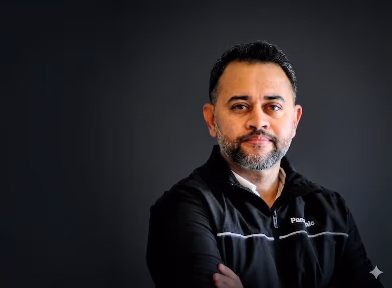 Man with short dark hair and beard wearing a black jacket against a dark background.