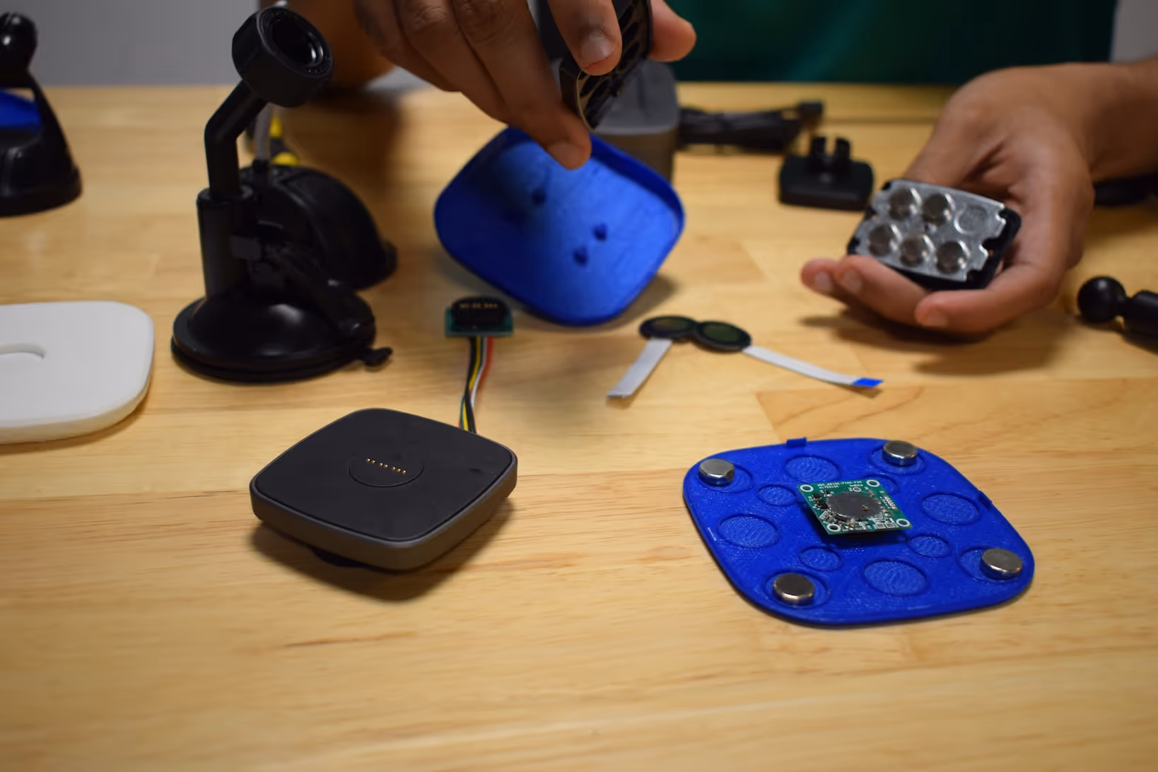 Hands assembling electronic components including circuit boards and blue 3D printed parts on a wooden table.