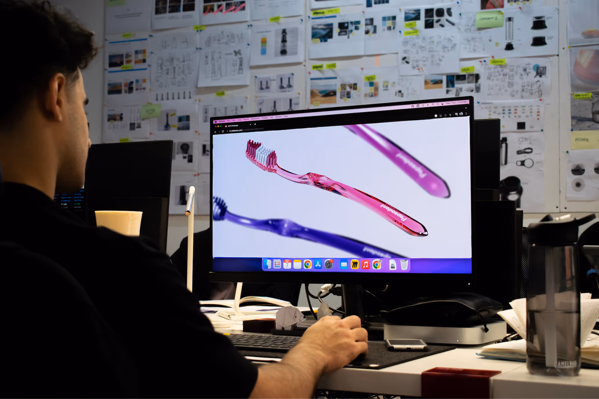 Person working at a desk with a computer displaying colorful toothbrush designs on screen in a design studio.