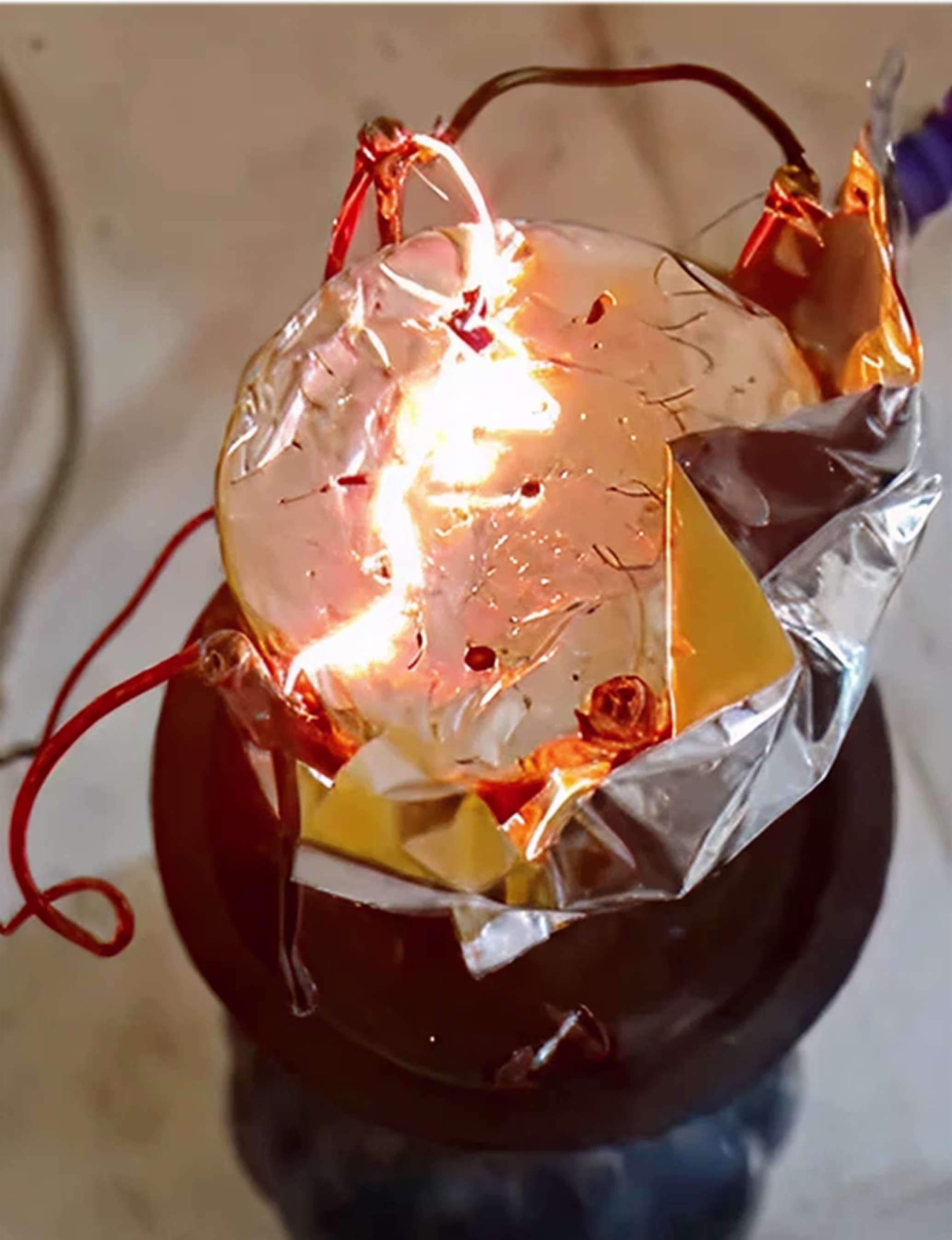 Bright electric arc inside a glass container with red wires and aluminum foil surrounding it.