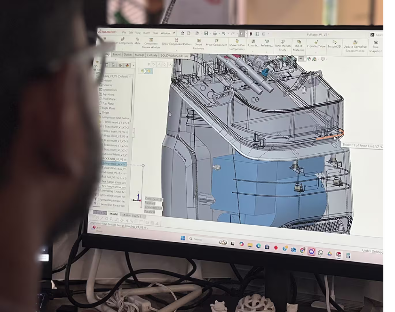 Person viewing a complex 3D mechanical design model on a computer screen using CAD software.