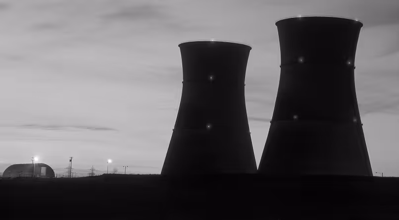 Silhouette of two cooling towers and a dome-shaped building at dusk with scattered lights.