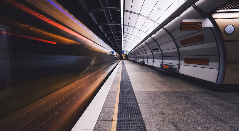 Blurred motion of a train speeding through a modern underground station with curved, white-paneled walls and empty platform.