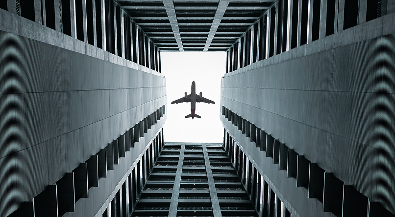 Airplane flying overhead viewed from the bottom of a tall rectangular building courtyard.