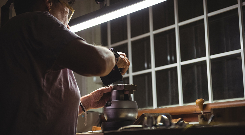 Person sharpening a tool or object using a grinding machine under a bright lamp near a window.