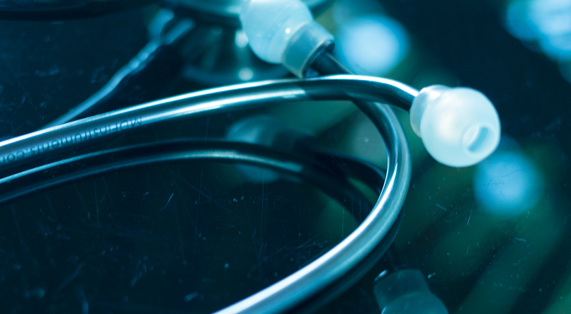 Close-up of a stethoscope resting on a reflective dark surface.