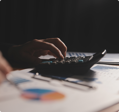 Person using a calculator on a desk with financial charts and graphs.
