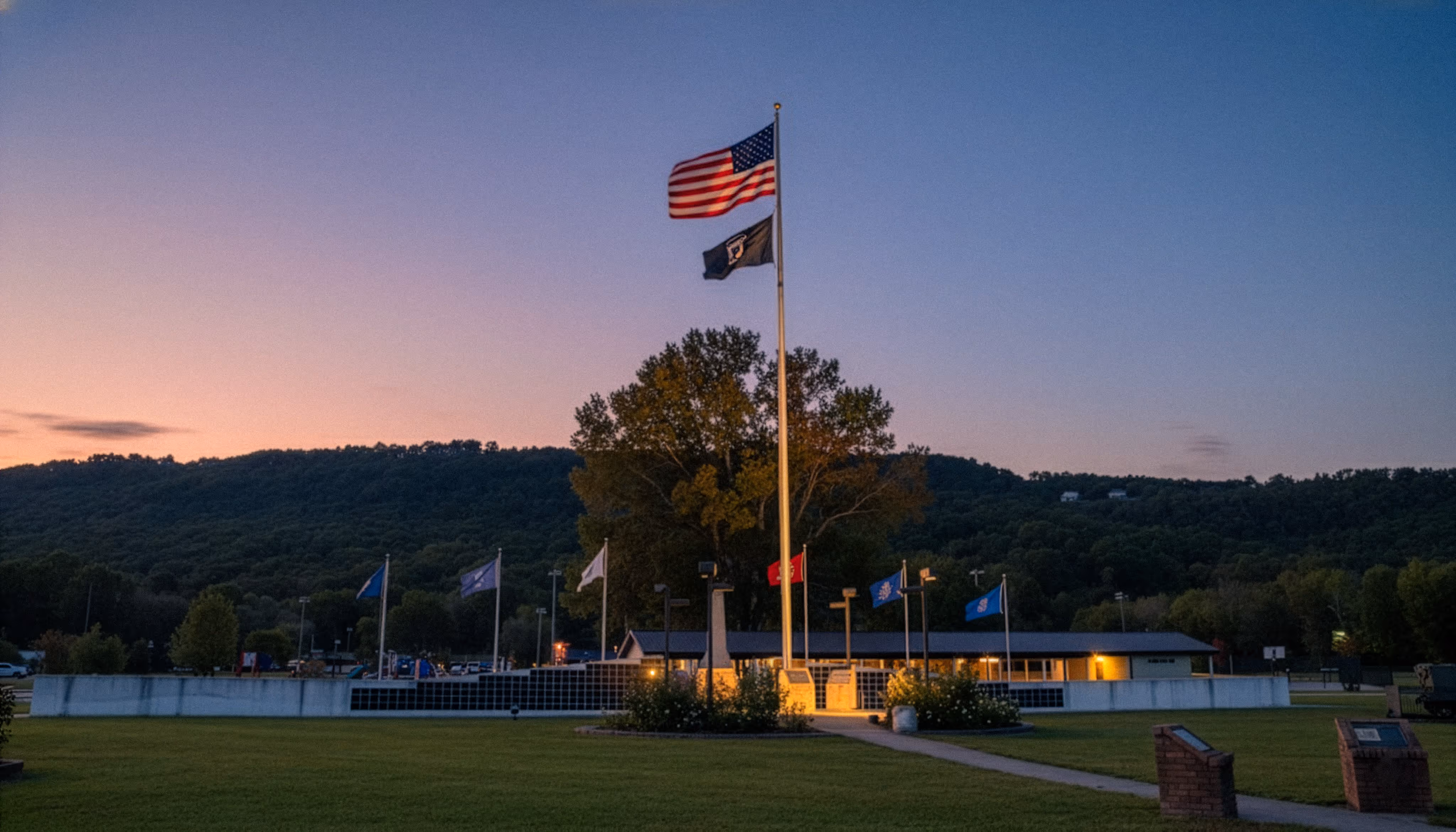 Evening view of Veterans Park in Soddy-Daisy, Tennessee, showing the American flag, memorial grounds, and hillside backdrop at dusk.