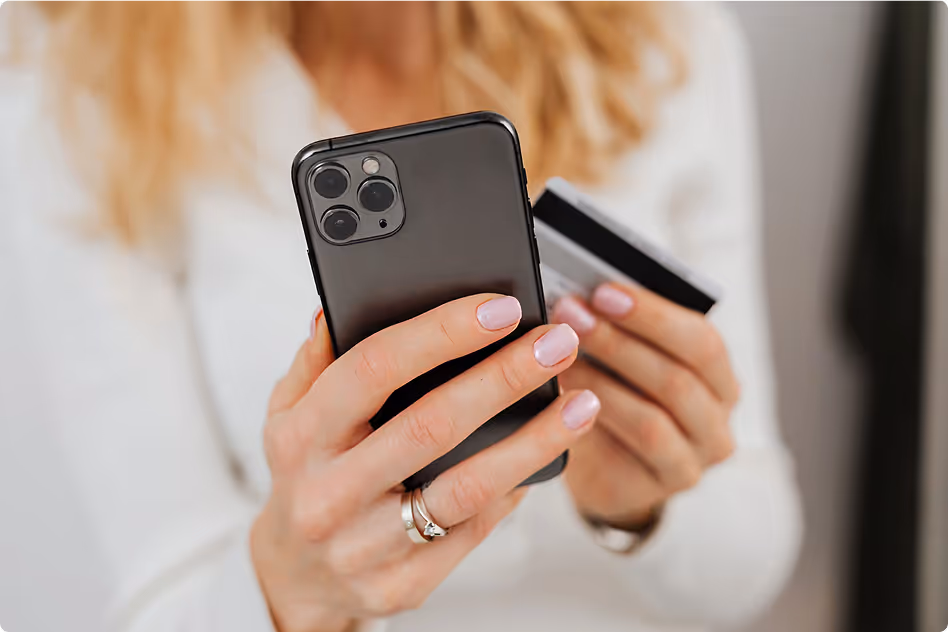 Nainen pitää mustaa älypuhelinta ja maksukorttia käsissään.