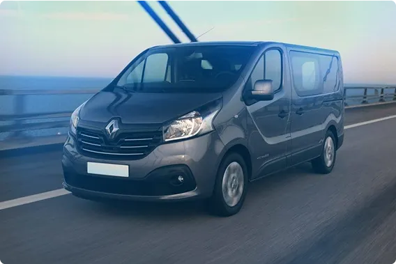 Sininen Renault-tavara-auto ajaa sillalla meren yllä hämärässä valaistuksessa.