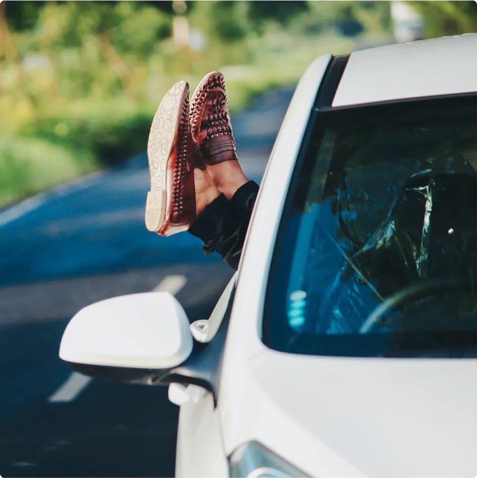 Jalat, joissa on ruskeat kengät, roikkuvat ulos valkoisen auton ikkunasta tielle päin.