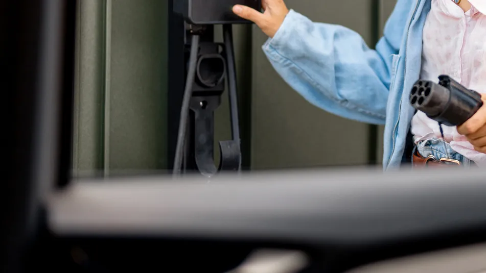 Henkilö kädessä sähköauton latausliitin ja laturin päässä oleva pistoke.