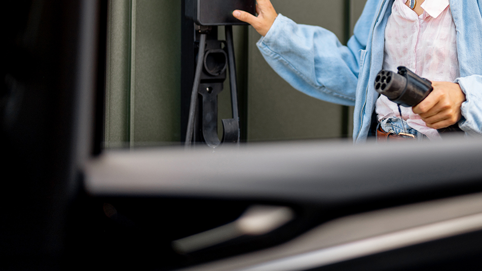 Henkilö pitää sähkönauton latausliitintä ja avaa latauspistokkeen luukkua.