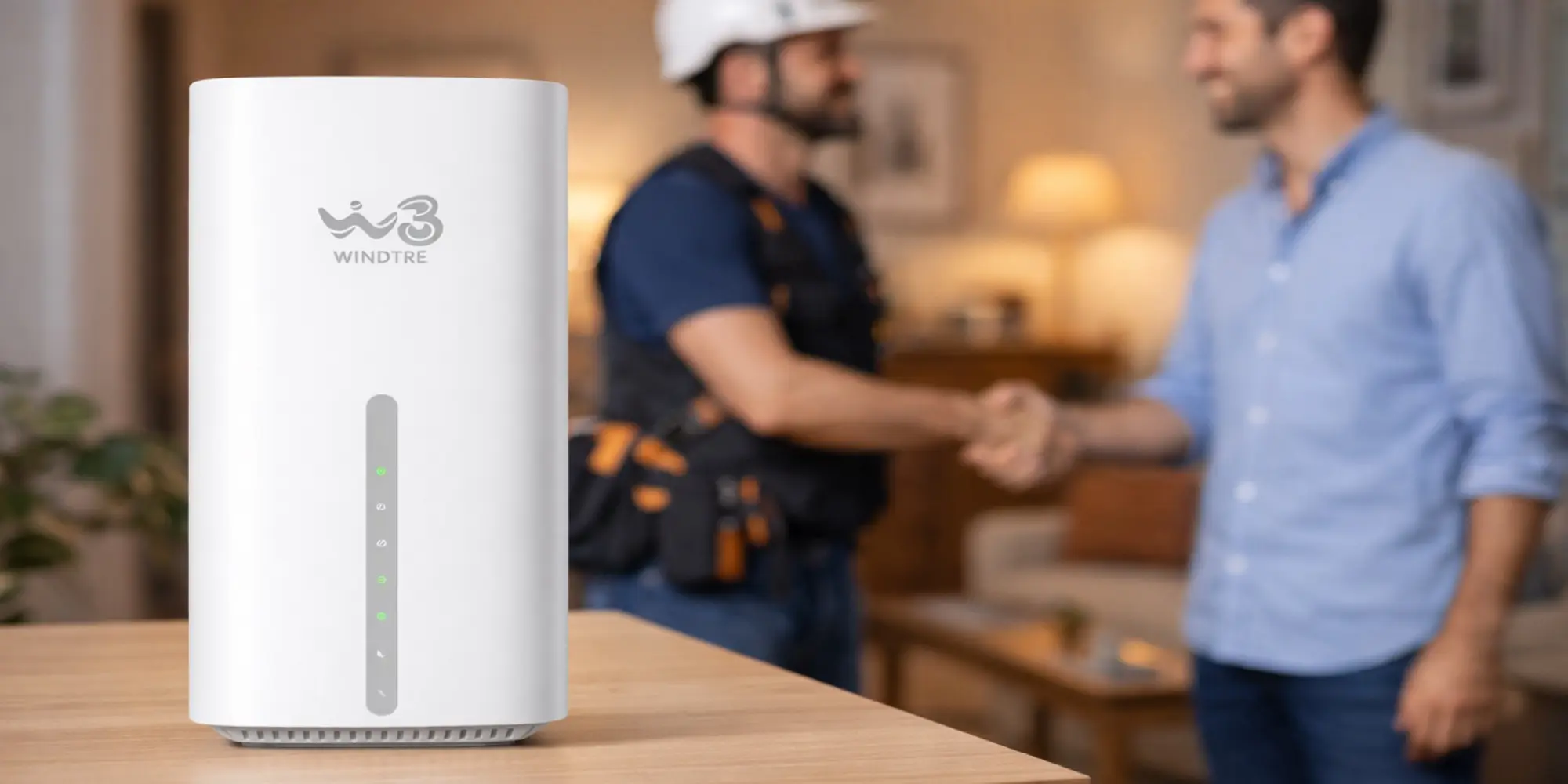 Router Windtre posizionato su un tavolo in primo piano, con tecnico e cliente che si stringono la mano sullo sfondo dopo un'installazione