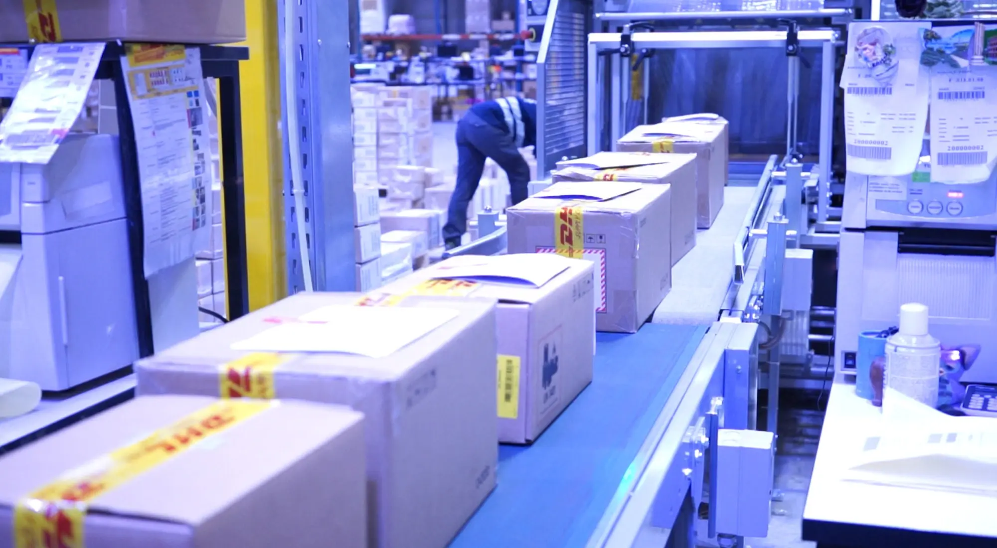 Nastro trasportatore in un centro logistico DHL con pacchi in lavorazione e operatore sullo sfondo
