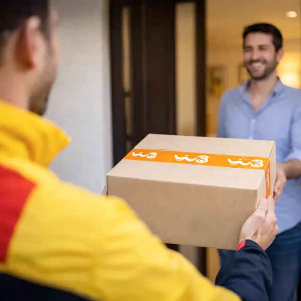 Corriere in divisa gialla consegna un pacco con nastro brandizzato WINDTRE a un cliente sorridente sulla soglia di casa