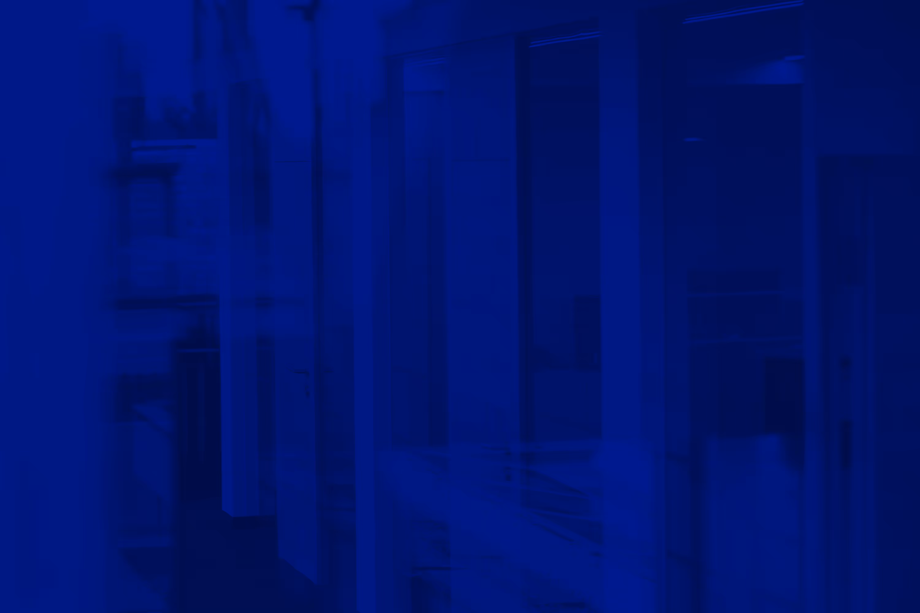 Gedimmtes blaues Bild eines Innenraums mit Glaswänden und Türen, möglicherweise ein Büro oder Flur.