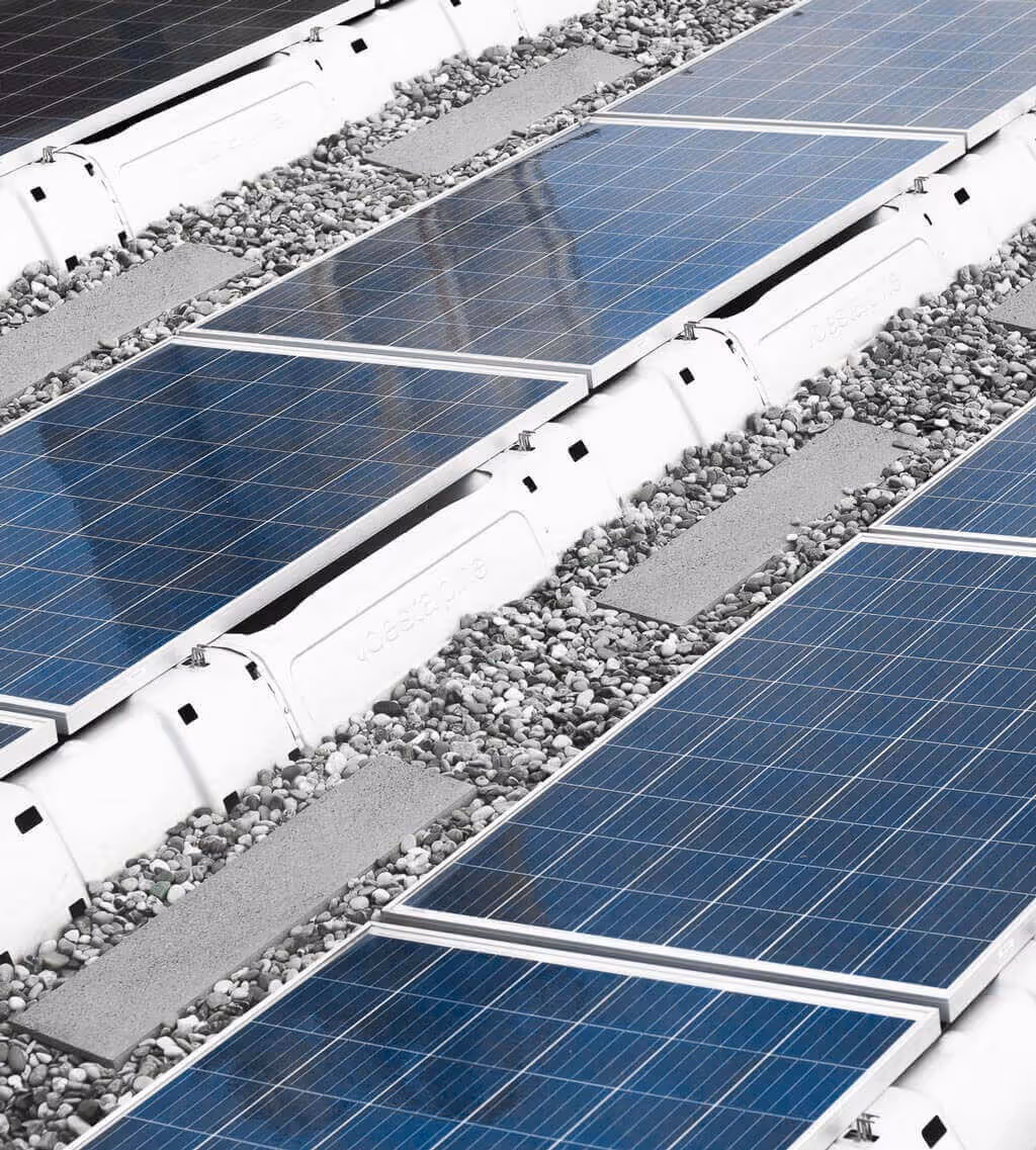 Reihen von blauen Solarmodulen, montiert auf einer weißen Struktur mit Kies dazwischen.