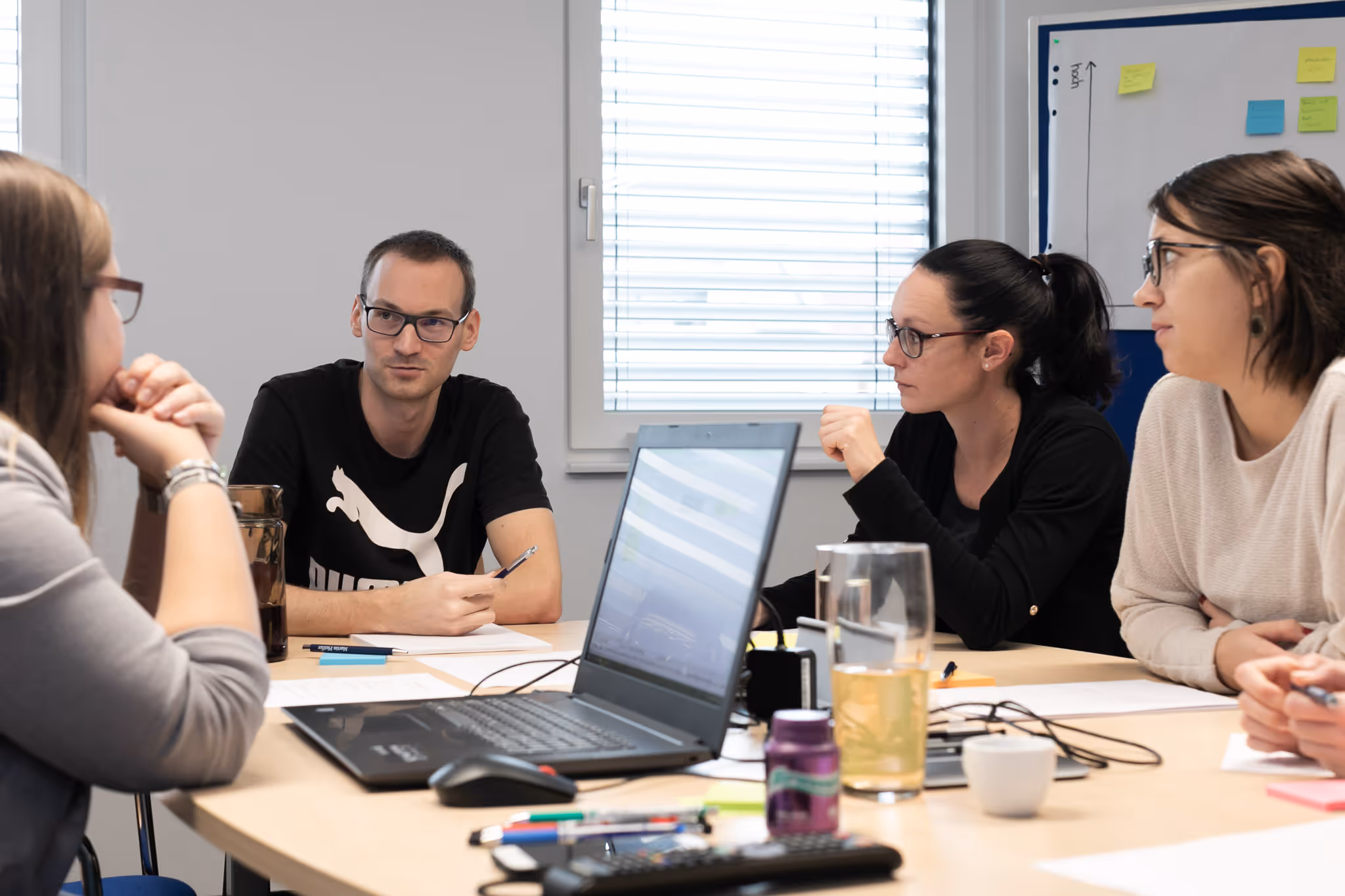 Vier Personen sitzen an einem Tisch und führen eine Besprechung in einem gut beleuchteten Raum.