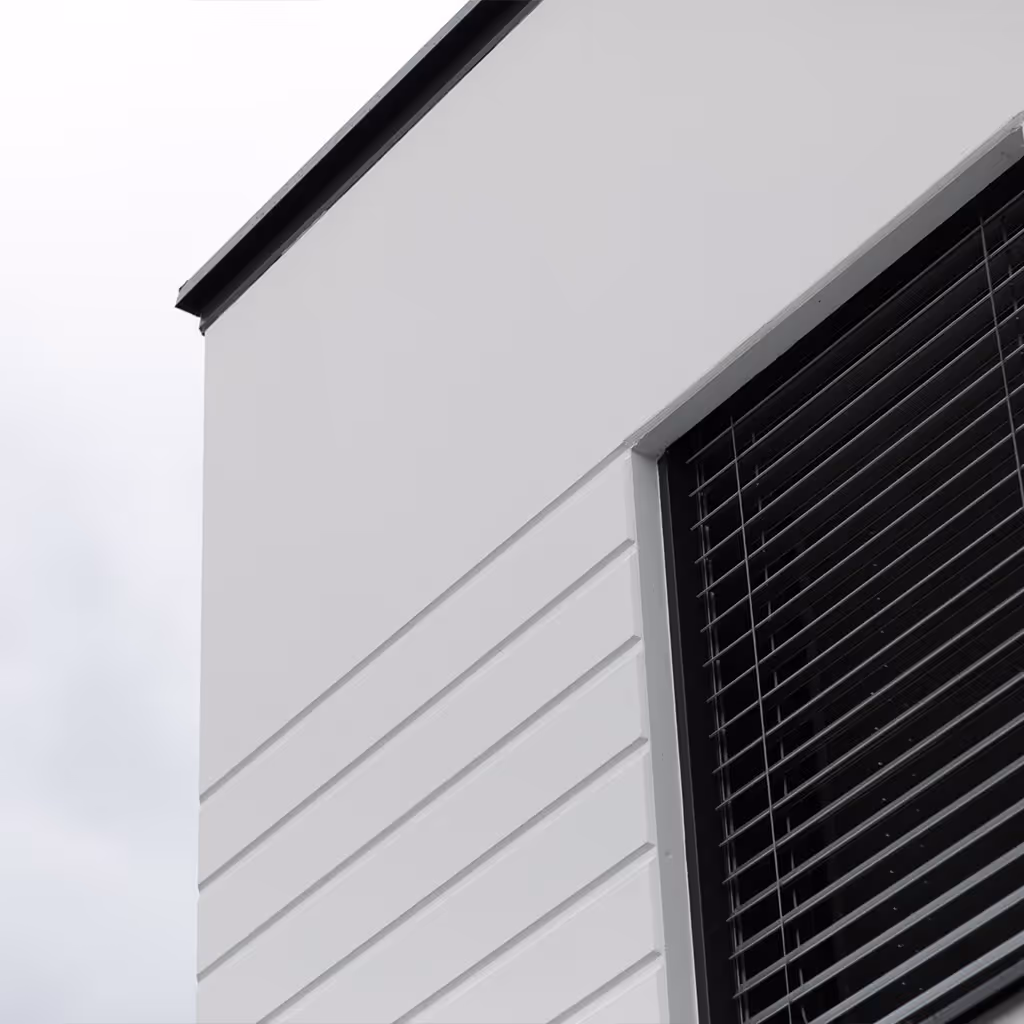 Moderne Gebäudeecke mit weißer Fassade und schwarzem Fenster mit horizontalen Jalousien.