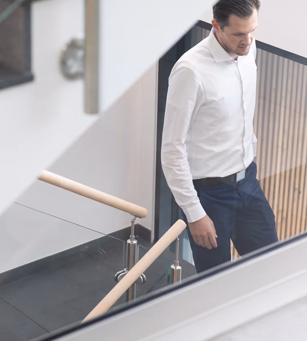 Geschäftsmann in weißem Hemd und dunkler Hose geht eine moderne Treppe mit Holzgeländer hinunter.