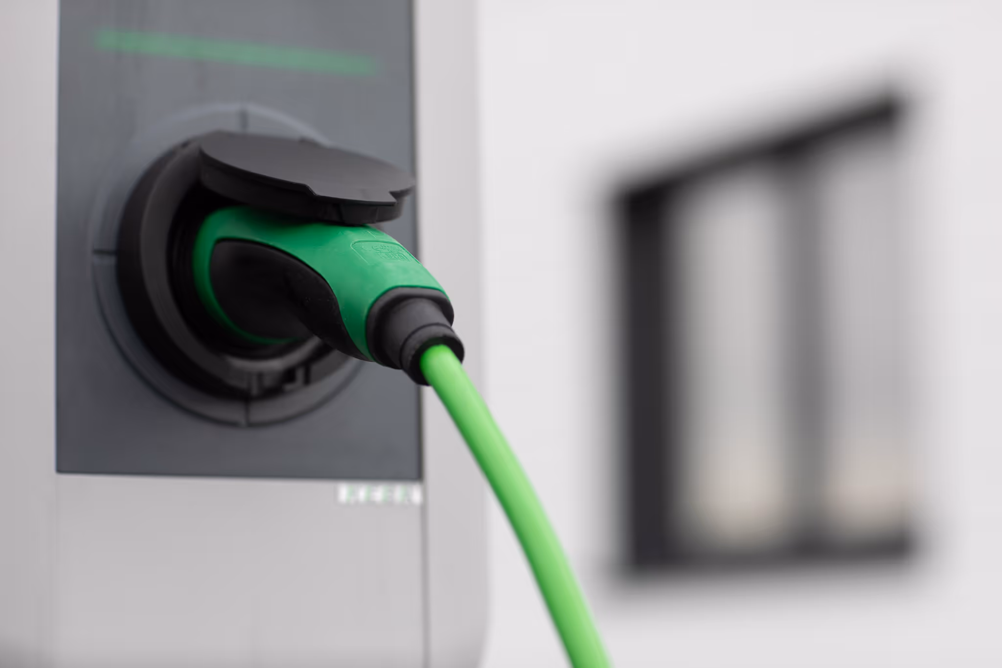 Nahaufnahme eines grünen Ladesteckers, der in eine graue Ladestation eingesteckt ist.