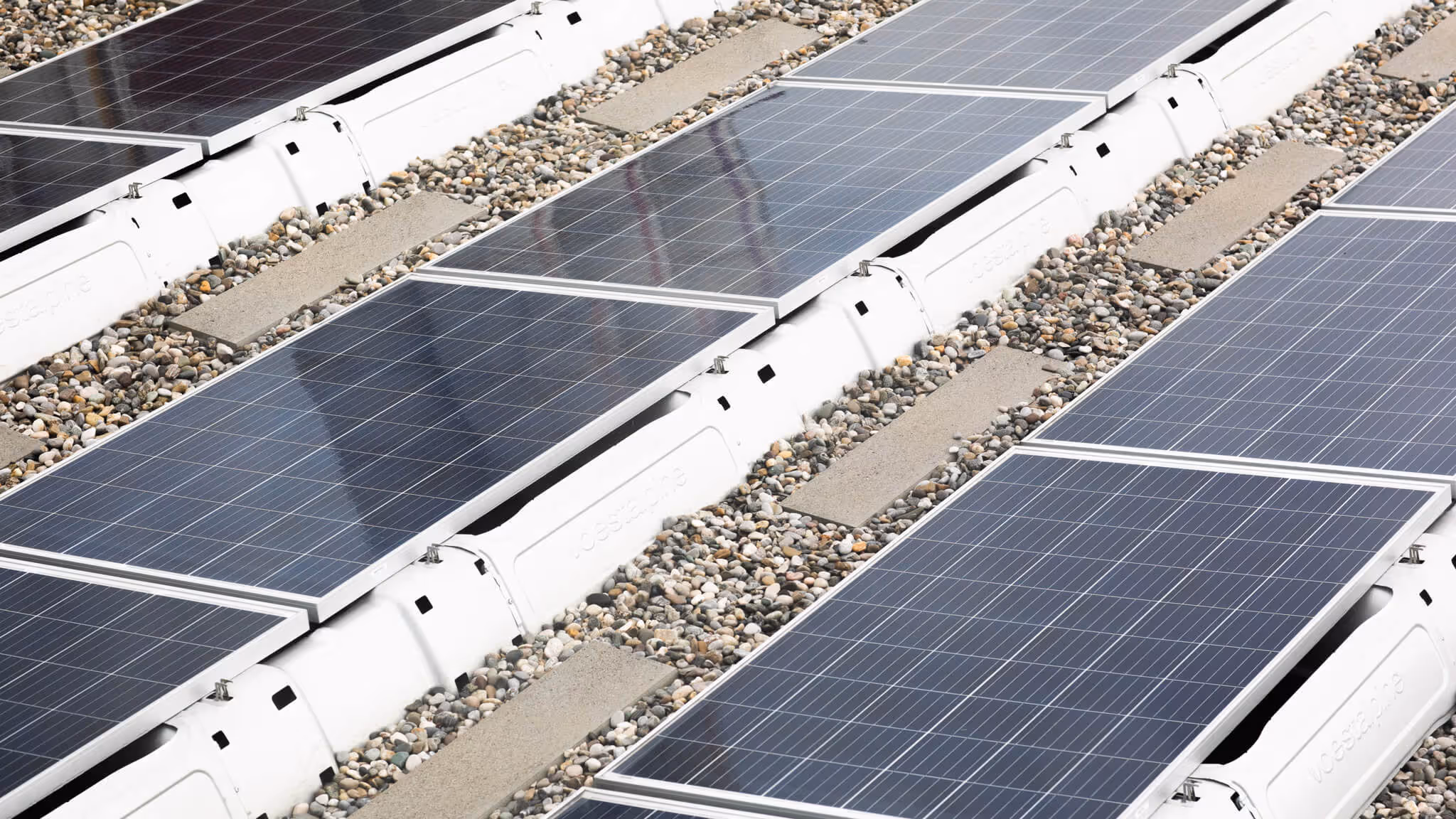 Dach mit mehreren Reihen von Solarpaneelen, die auf weißen Halterungen über einem Kiesdach montiert sind.