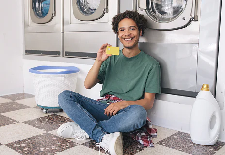 Jeune assis dans une laverie montrant sa carte de crédit