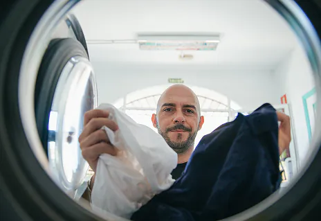 Un homme qui pose son linge dans le tambour d'une machine à laver