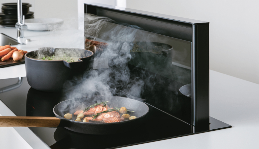 Dampfender Topf und Pfanne mit Lachs auf Induktionskochfeld – moderne Küche mit innovativer Dunstabzugstechnik und hochwertiger Küchenausstattung von Küche Aktiv.