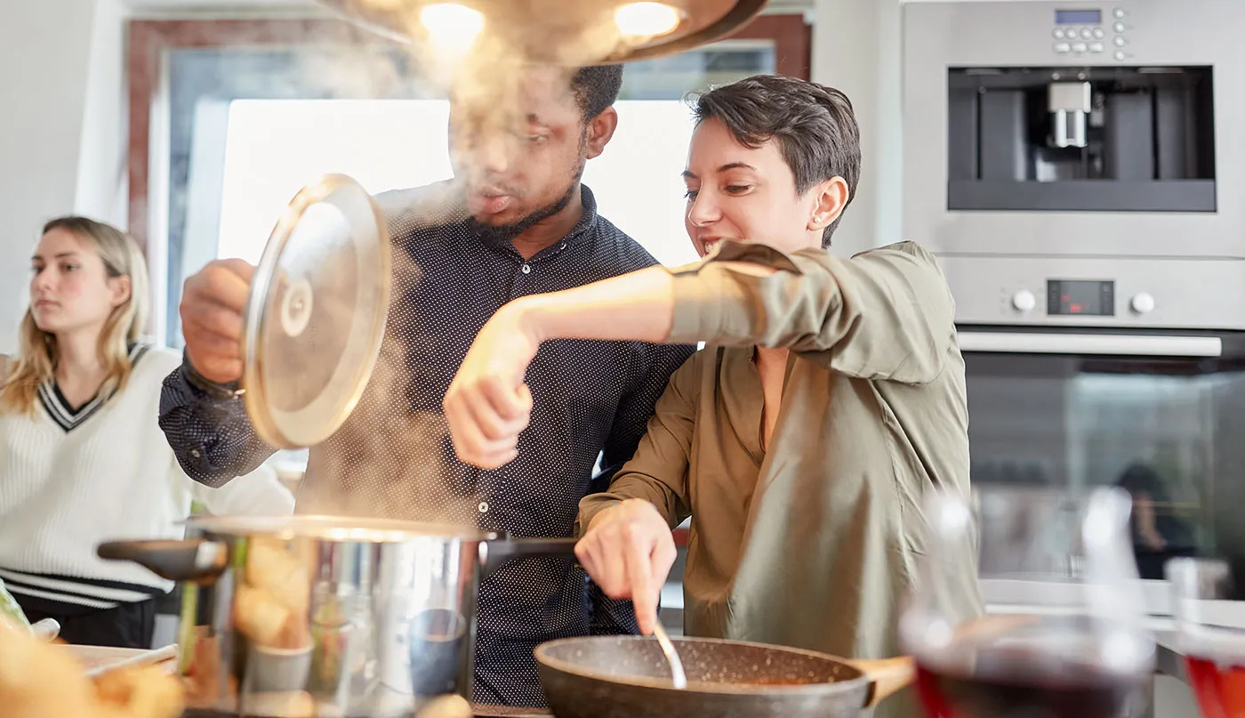 Zwei Personen kochen gemeinsam in einer modernen Küche, rühren in Töpfen und Pfannen und genießen das gemeinsame Kocherlebnis – authentische Küchenszene voller Freude und Genussmomente beim Kochen zu Hause.
