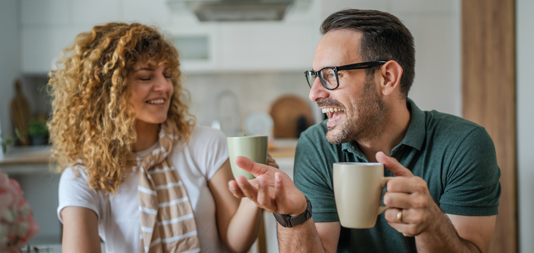 Ein lachendes Paar genießt gemeinsam eine Tasse Kaffee in einer modernen Küche. Die gemütliche Atmosphäre und das natürliche Licht vermitteln Lebensfreude, Entspannung und harmonisches Küchendesign.