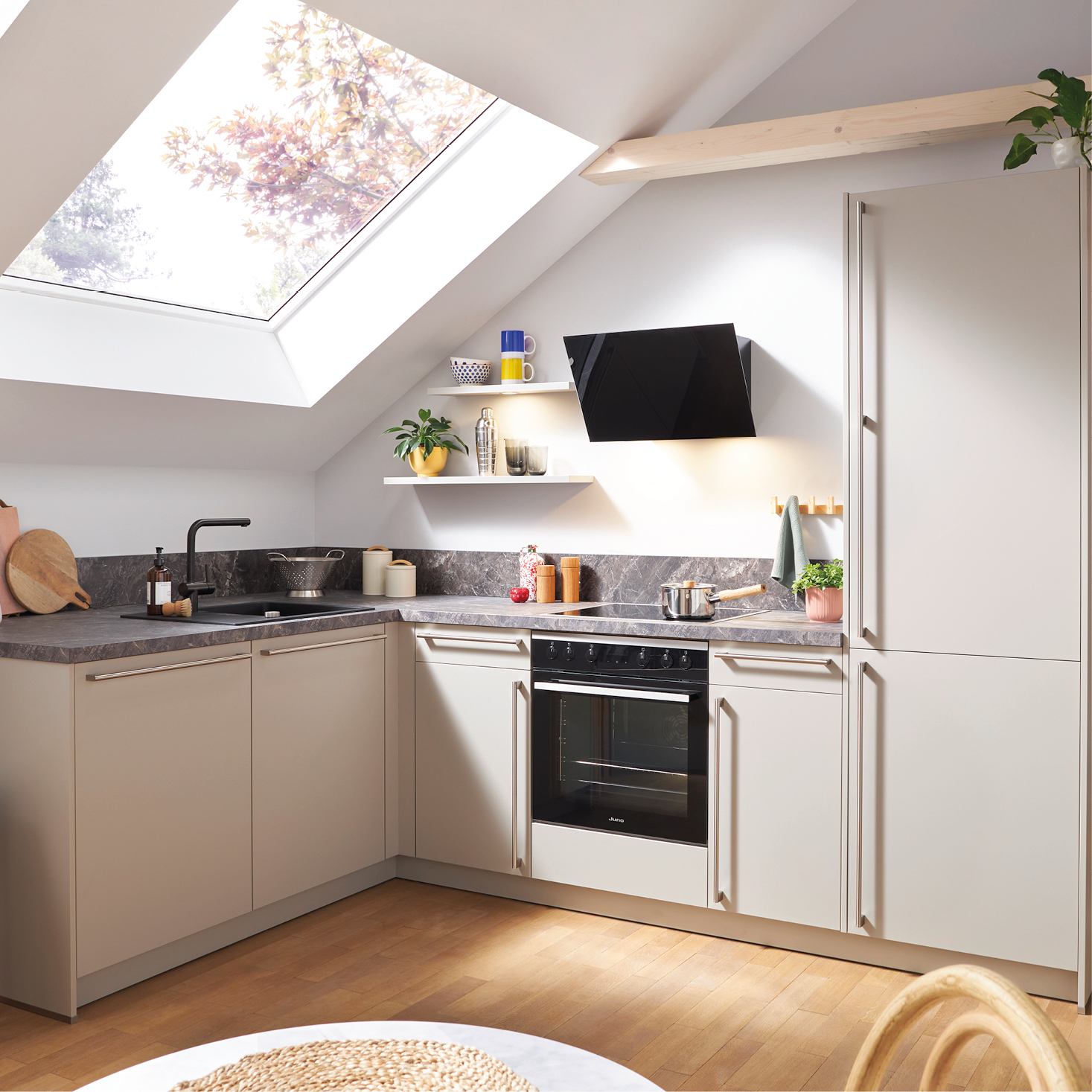 Helle moderne Küche unter Dachschräge mit großem Dachfenster, grauen Fronten und Naturstein-Arbeitsplatte – stilvolle Küchengestaltung mit viel Tageslicht und wohnlicher Atmosphäre.