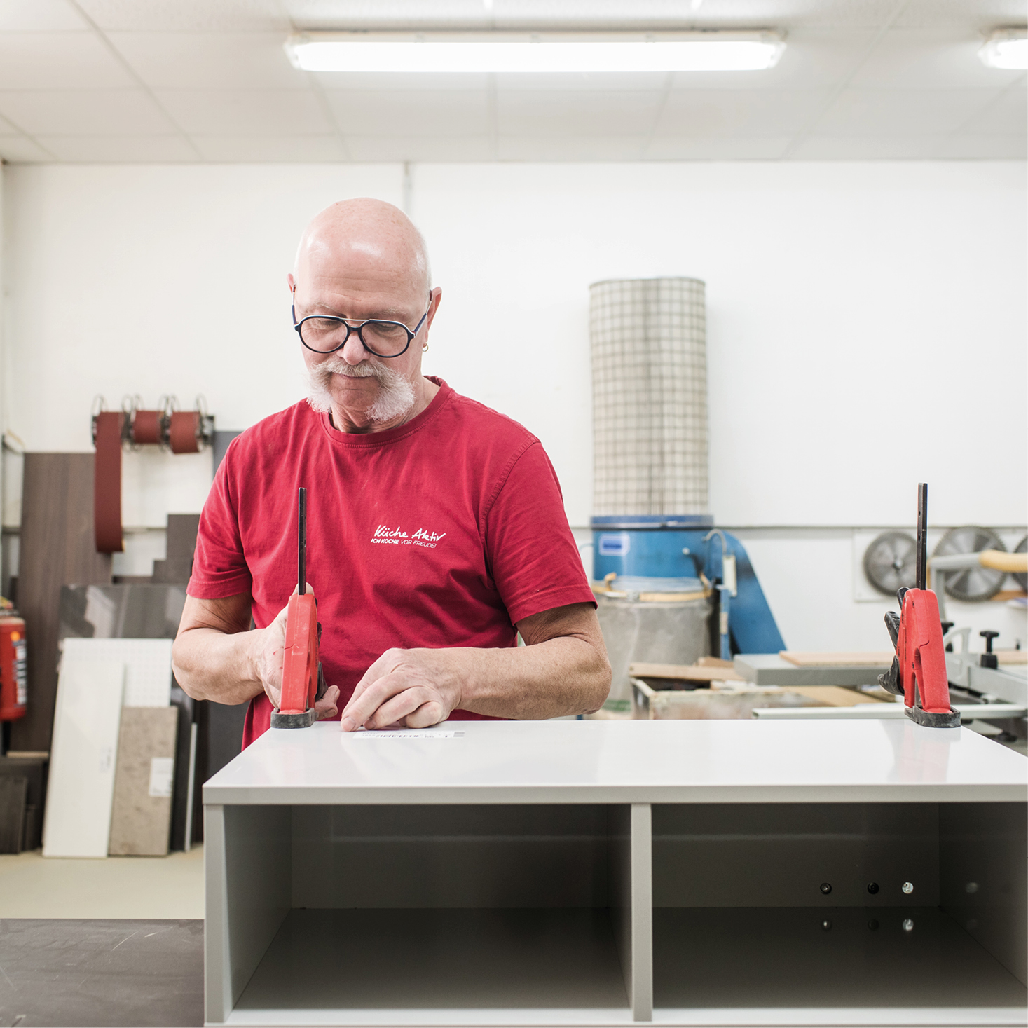 Handwerker in rotem Küche Aktiv Shirt bei der Küchenmontage – präzise Schreinerarbeit in moderner Werkstatt für maßgefertigte Küchenmöbel.