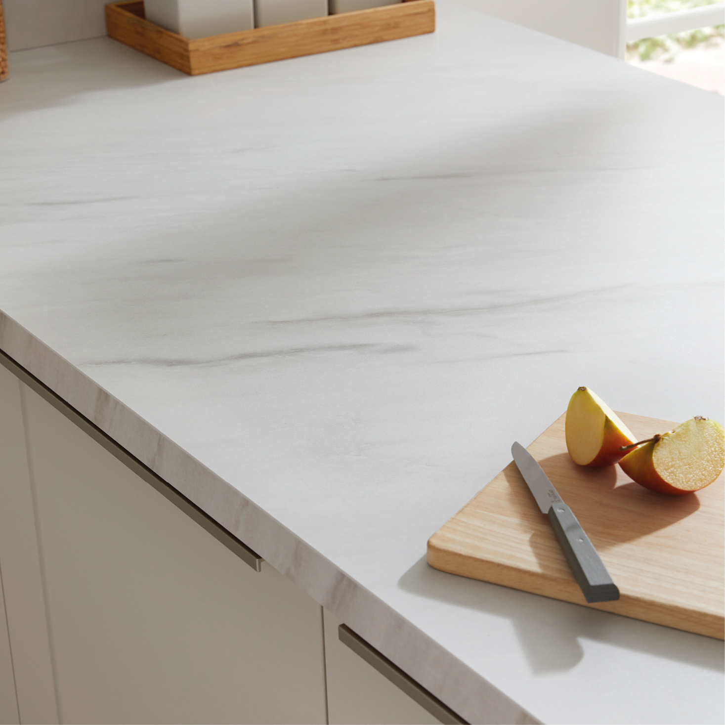 Detailaufnahme einer hellen Küchenarbeitsplatte mit Marmoroptik – hochwertige Küchenoberfläche mit Holzbrett, Messer und Apfelstücken für modernes Küchendesign.