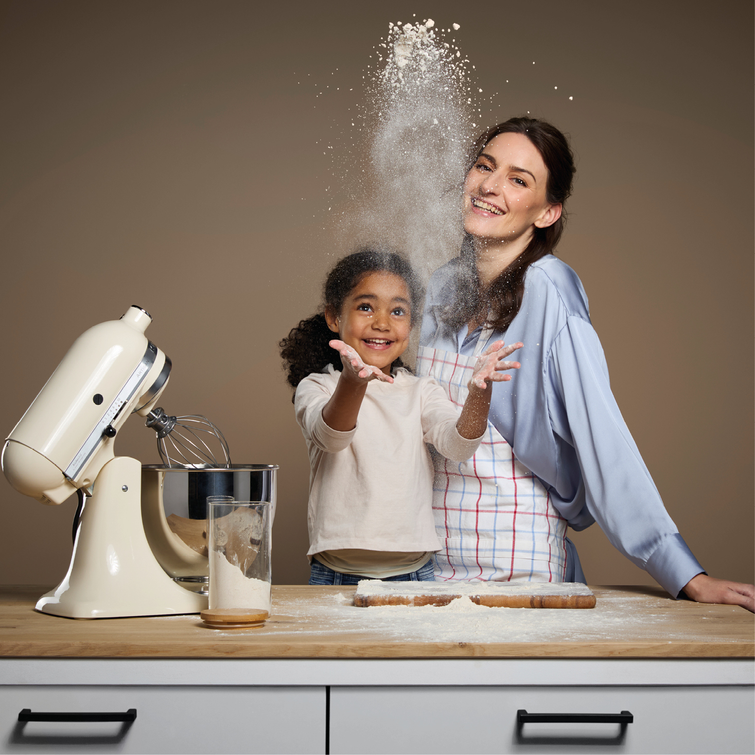 Mutter und Tochter haben Spaß beim Backen in moderner Küche – Kind wirft Mehl in die Luft, während die Mutter lacht. Symbol für Freude, Familienzeit und gemeinsames Backvergnügen in der Küche.