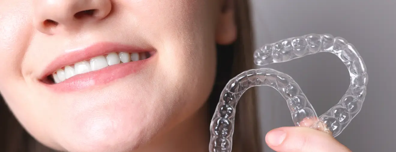 Close-up of a smiling person holding clear orthodontic aligners.