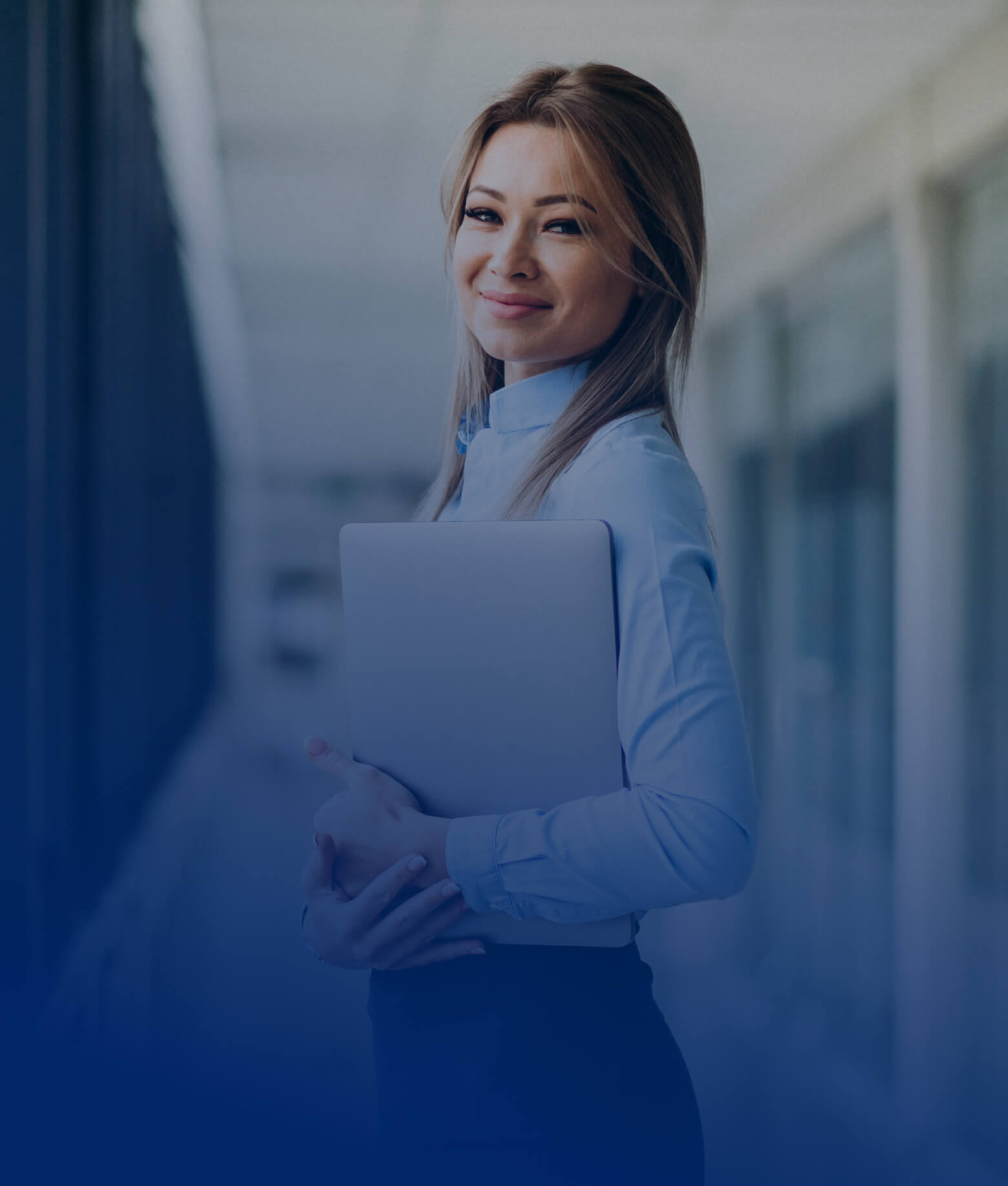Lächelnde Geschäftsfrau im hellblauen Hemd, die einen Laptop vor dem Bauch hält.