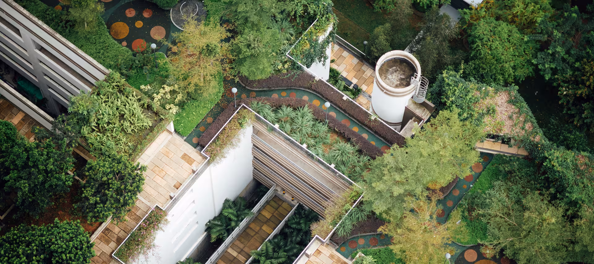 Aerial view of a futuristic-style building, with abundant greenery and trees within and around the building. 