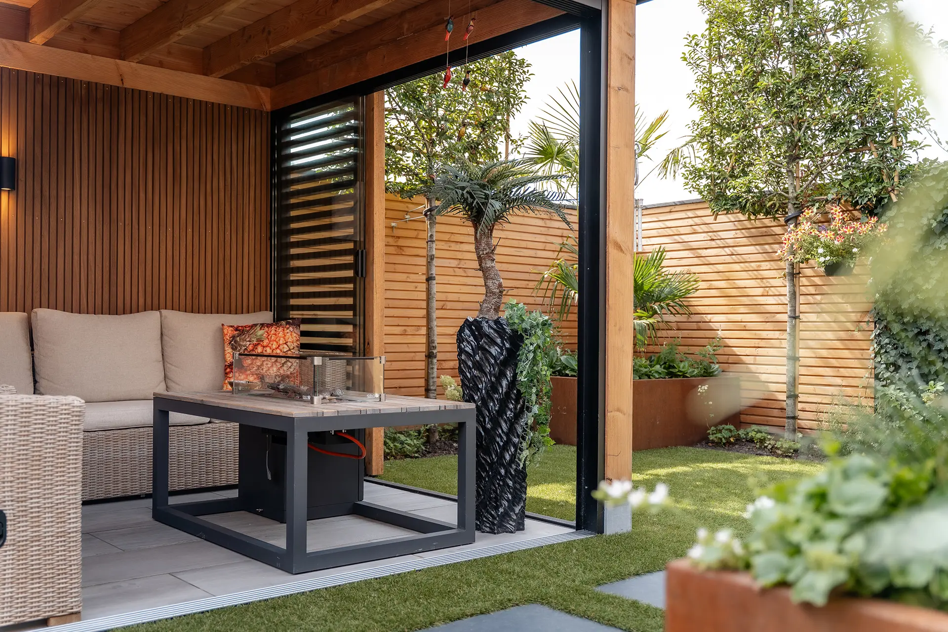 In Blokker hebben we deze tuin mogen aanleggen rondom een grote veranda. De bewoners wilden graag een onderhoudsarme tuin met een gezellige patiosfeer. Een plek waar je het hele jaar door fijn kunt zitten. Er is gewerkt met warme materialen zoals hout en cortenstaal, gecombineerd met kunstgras voor een strak en praktisch resultaat. De watertafel zorgt voor leven in de tuin en maakt het geheel helemaal af. Bij de oprit hebben we gespeeld met verschillende tegelformaten, waardoor het een speels en eigen karakter kreeg. Een tuin met sfeer, praktisch in onderhoud en precies zoals de bewoners het voor ogen hadden.