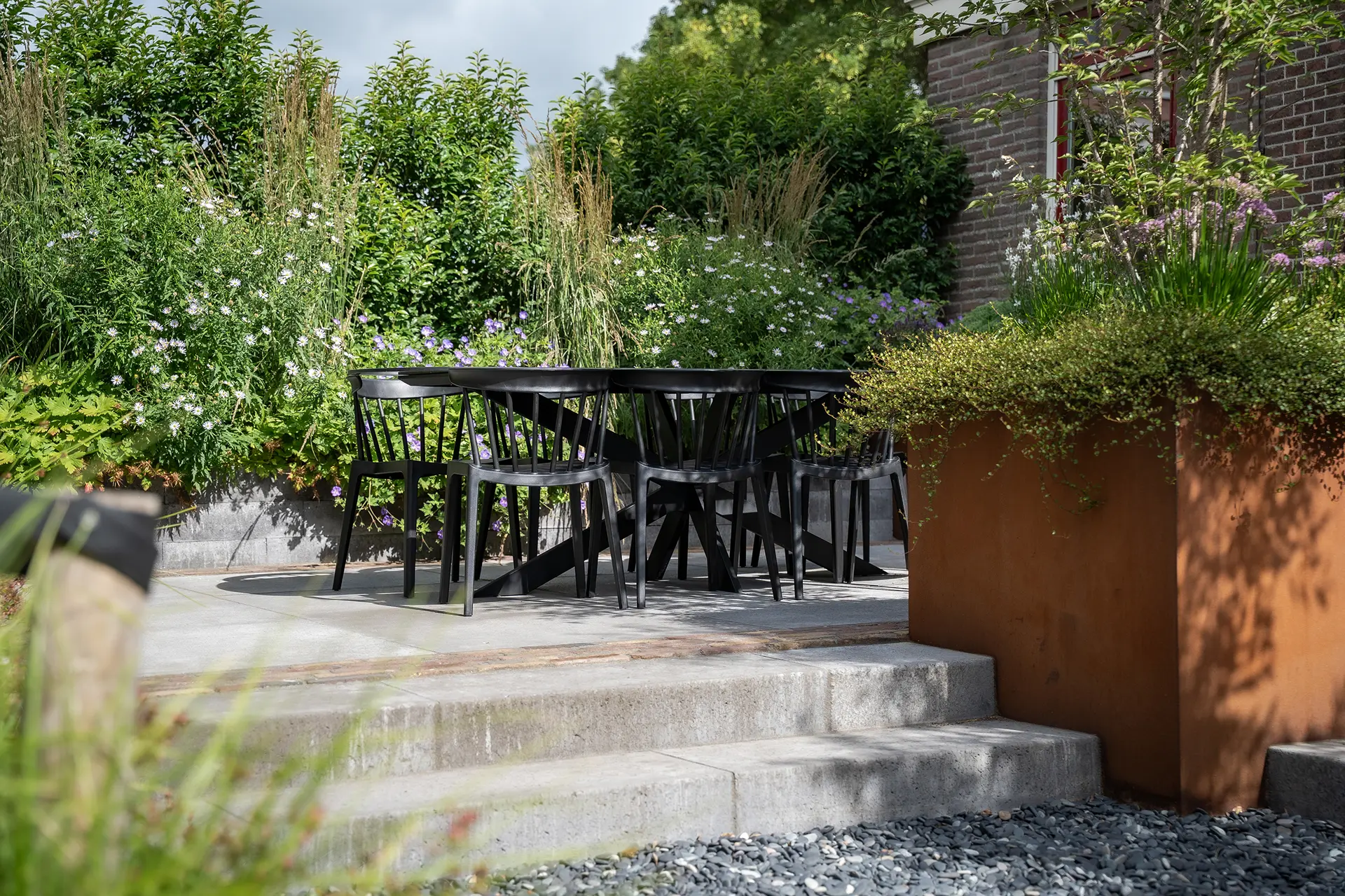 In deze binnentuin hebben we gewerkt aan een ontwerp dat past bij het karakter van het rijksmonumentale pand. De tuin heeft een creatieve indeling met verschillende hoogtes en een mooie mix van materialen. Klinkers met een authentieke uitstraling, Schellevis tegels, grind, metselwerk, hout en cortenstaal zorgen samen voor een stoer en sfeervol geheel. De erfafscheiding is uitgevoerd met een op maat gemaakt hekwerk dat perfect aansluit bij de stijl van het pand. Zo is het een tuin geworden met stadse allure, maar ook met warmte en groen. Een plek waar materialen, vormen en details samen een kloppend geheel vormen.
